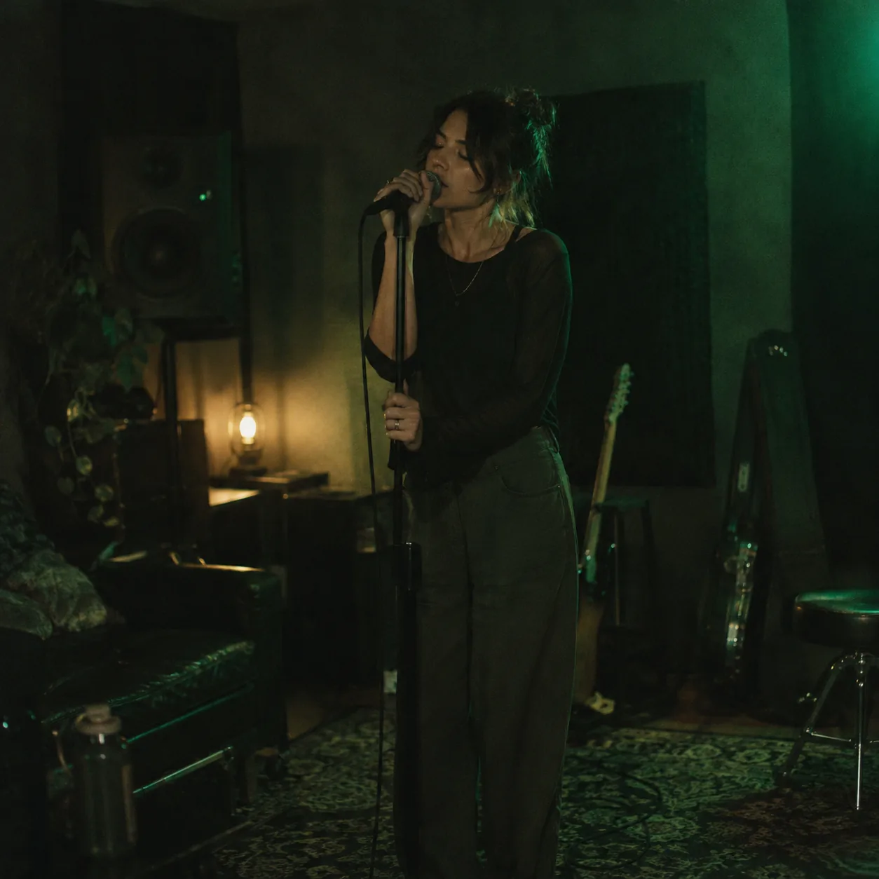 A singer rehearsing alone at a microphone over a backing track in a dim practice room