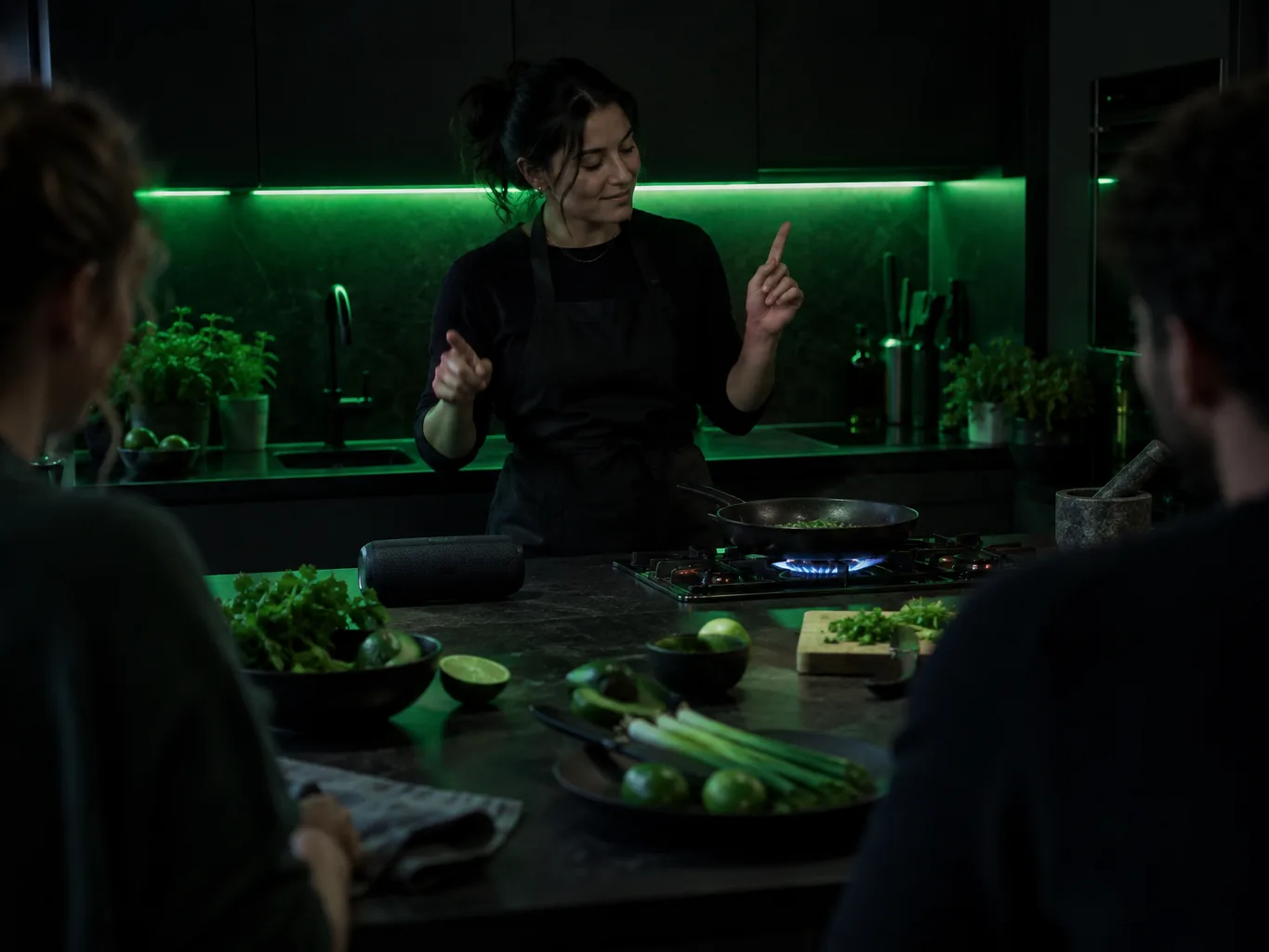 Cooking class teacher counting a beat behind a dark demo counter with a pan on a blue gas flame while students watch
